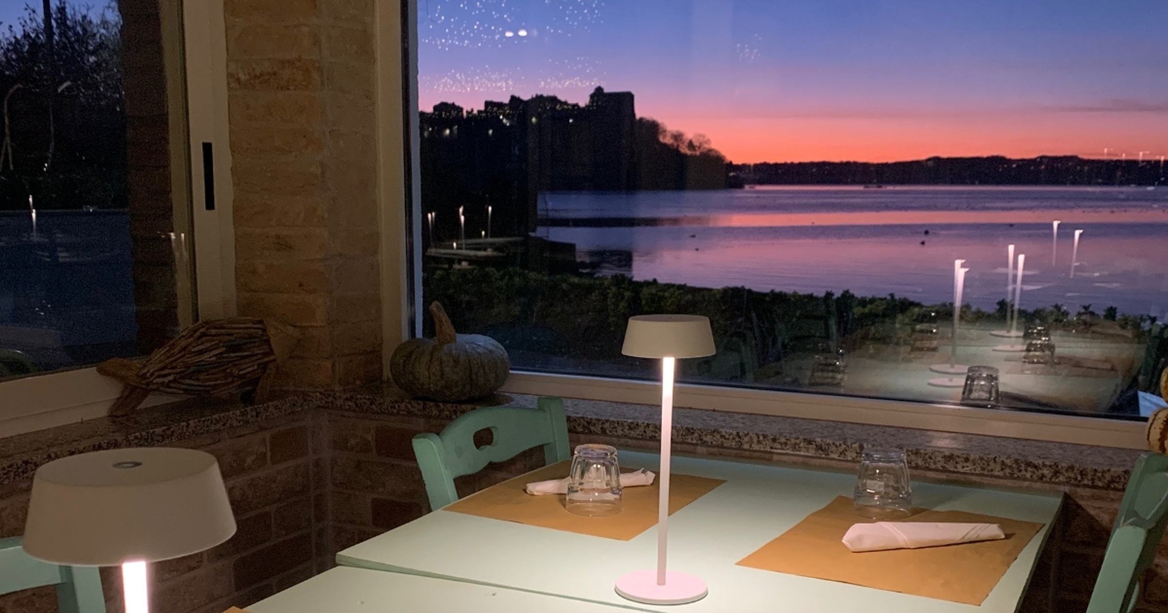 Tavolo apparecchiato con lampada e vista tramonto sul lago